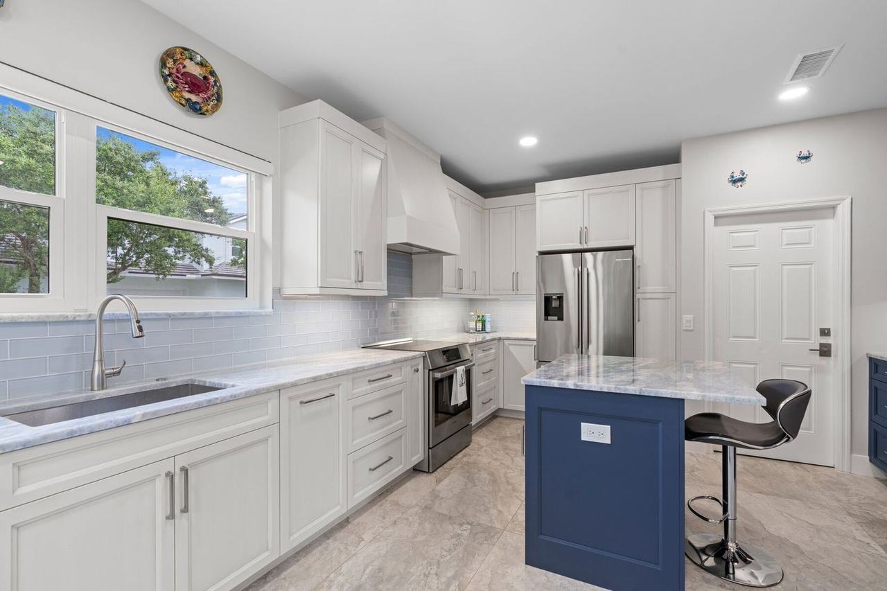 Renovated kitchen with white cabinetry, Azul Calcite counters and a navy island